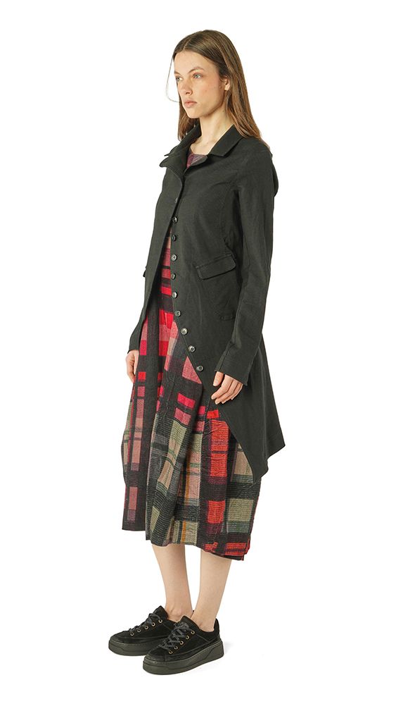 Frau trägt langen schwarzen Mantel über kariertem Kleid, schwarze Sneakers.