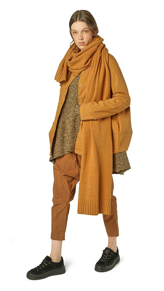 Frau trägt oversized beige Strickjacke mit Schal, braunen Strumpfhose und schwarzen Sneakern.