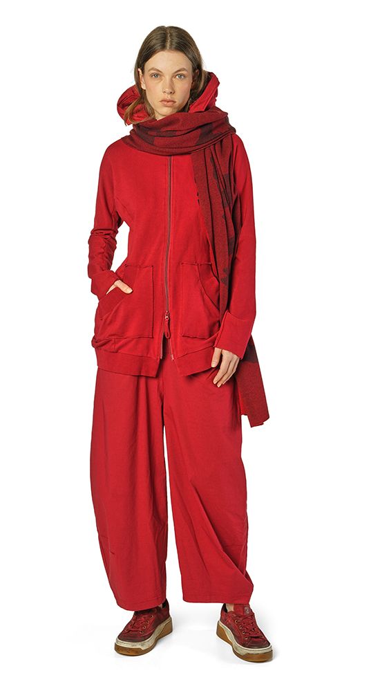 Frau trägt oversized roten Hoodie mit weitem Beinanzug und Schal, steht lässig auf hellem Untergrund.