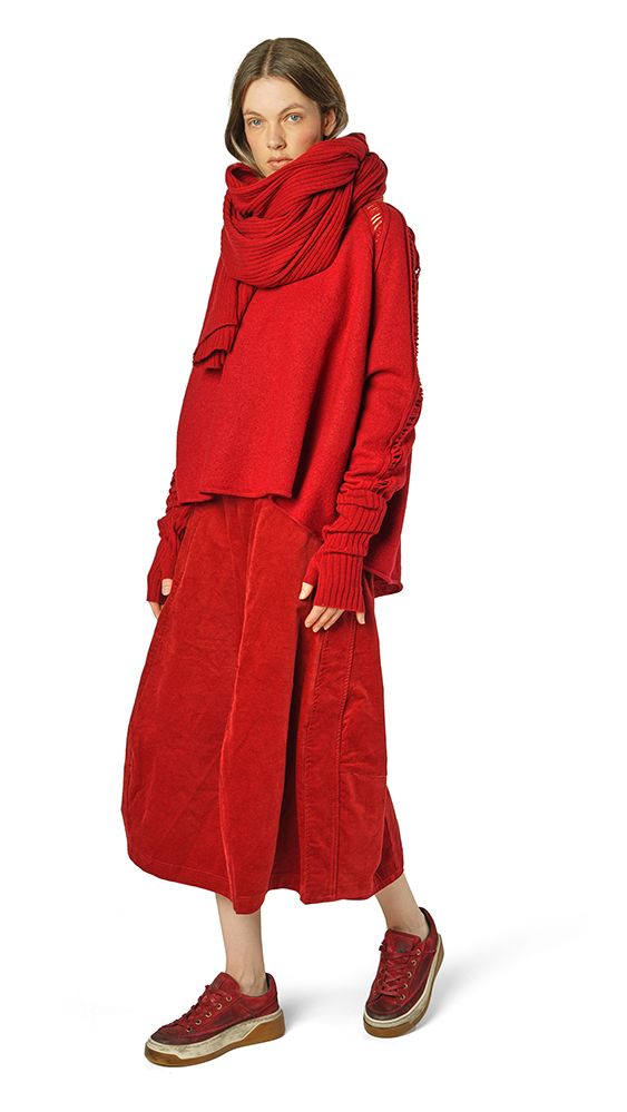 Frau trägt oversized roten Cordmantel mit Schal und beigen Sneakern.