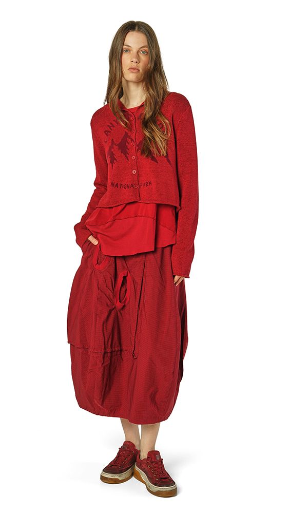 Frau trägt oversized rotes Ensemble mit weitem Rock und Sneakern, elegant-lässiger Stil.