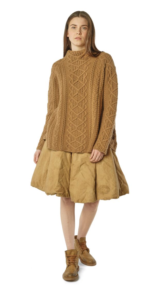 Frau trägt beige, oversized Strickpullover mit kurzem, weitem Rock und braunen Stiefeln.