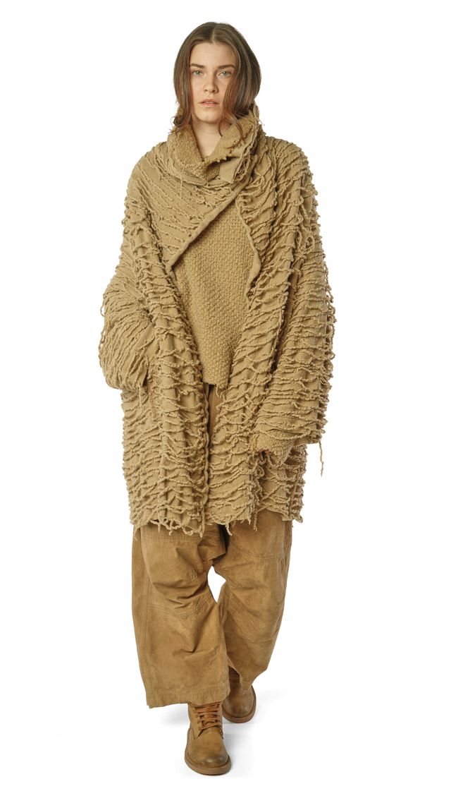 Person trägt oversized beige Strickponcho mit weiten Hosen und Stiefeln.