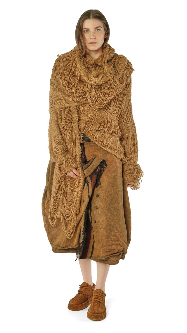 Frau trägt langes, texturiertes Kamelcoat-Outfit mit Fransen und braunen Stiefeln.