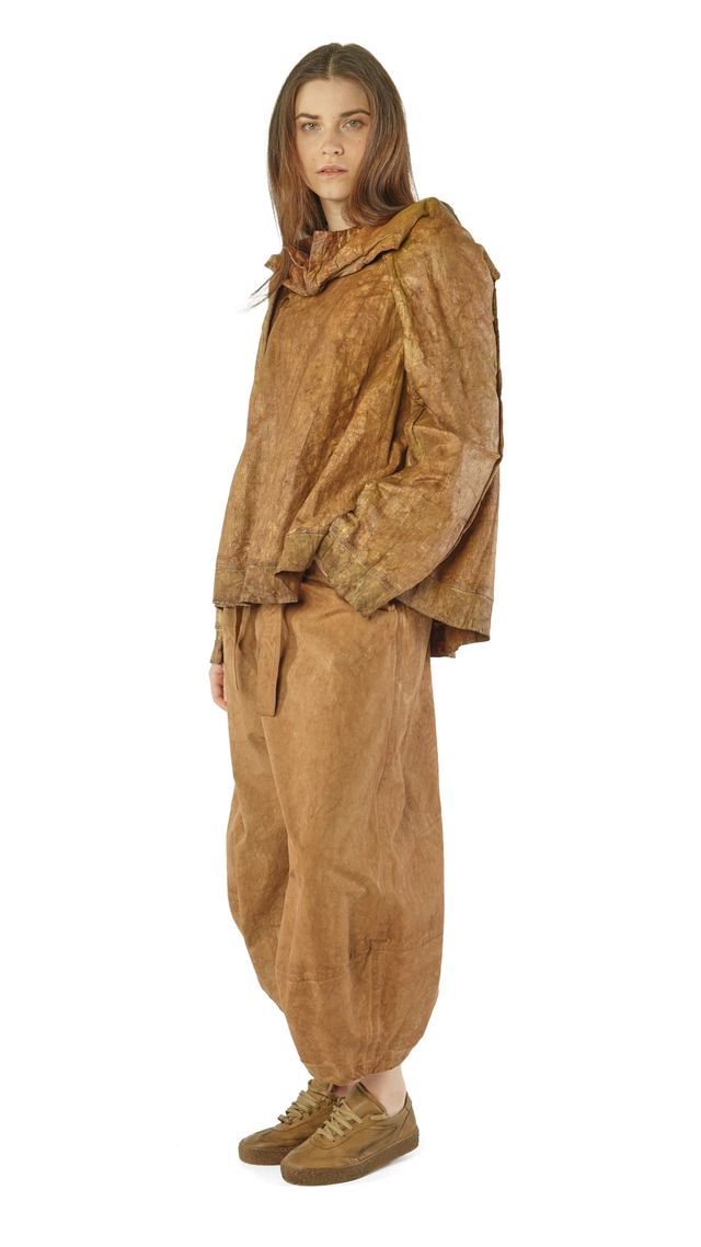 Person trägt oversized beige Leinen-Kombi aus Jacke und weiten Hosen, barfuß mit Sneakern.