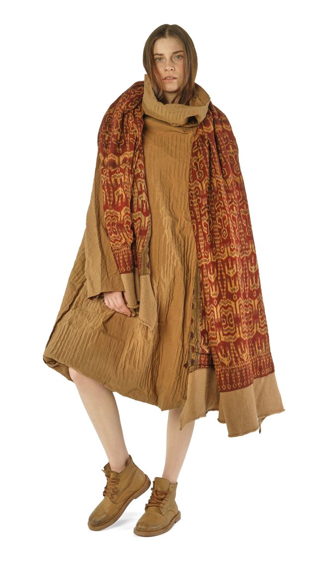 Person trägt langes, gemustertes Cape mit beige-gestreiftem Unterteil und robusten Stiefeln.