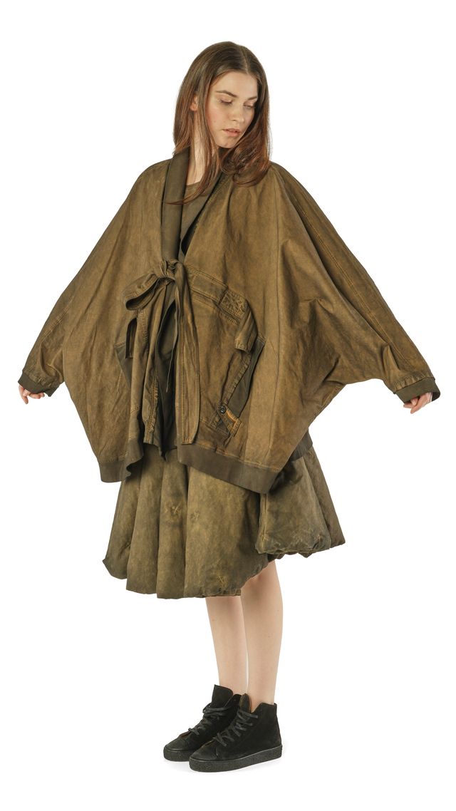 Frau trägt oversized olivgrünen Poncho mit schwarzem Gürtel und schwarzen Sneakern.