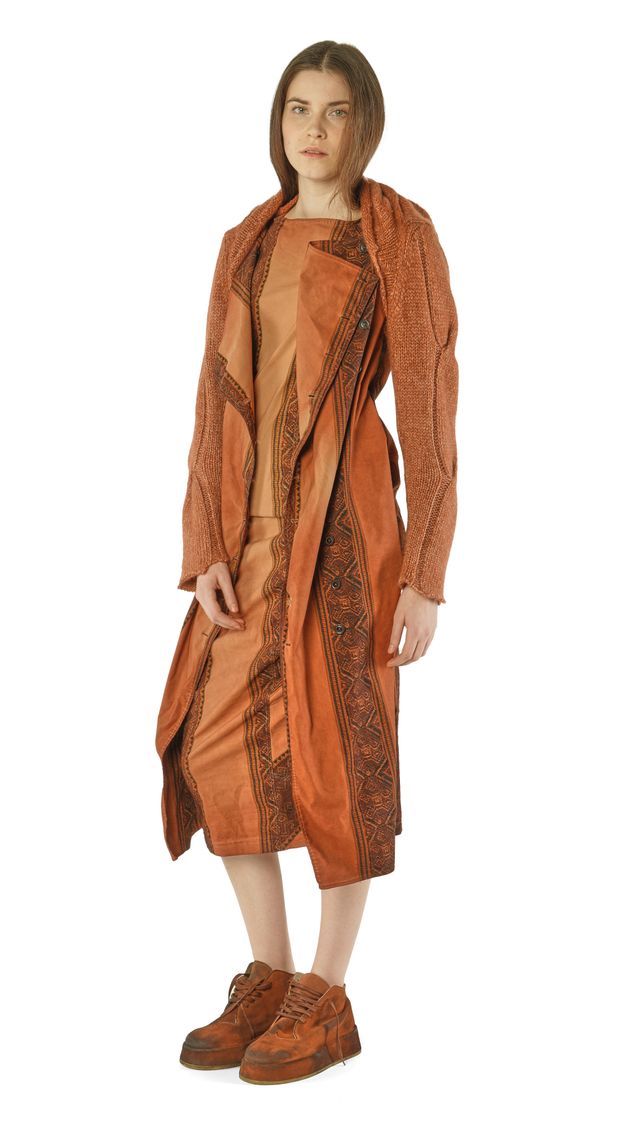 Frau trägt langes, ornamentales braunes Kleid mit Schal und robusten Stiefeln, elegant-bohemien Stil.