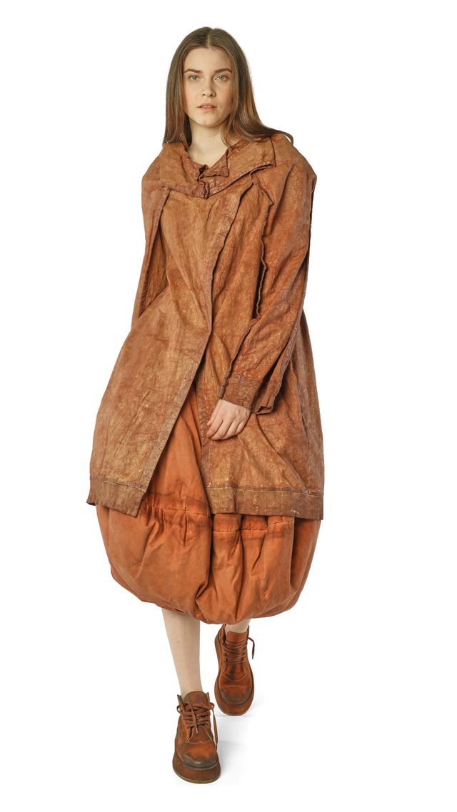 Frau trägt oversized braunes Lederkleid mit weitem Cape und robusten Stiefeln.