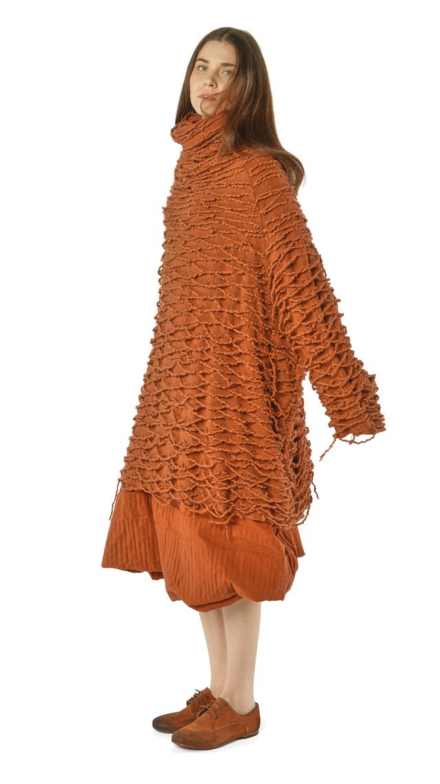 Frau trägt rustikalen, orangefarbenen Strickmantel mit weitem Schnitt und Paillettenrock, barfuß mit Schuhen.