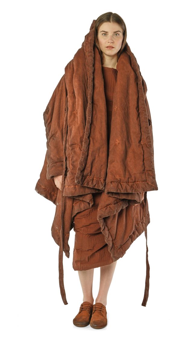 Person trägt altmodisches, braunes, langes Wollkleid mit Kapuze und Sandalen.