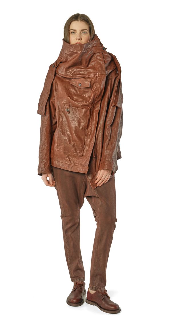Person trägt oversized braunes Leder-Outfit mit weitem Mantel und geraden Hosen, kombiniert mit Stiefeln.