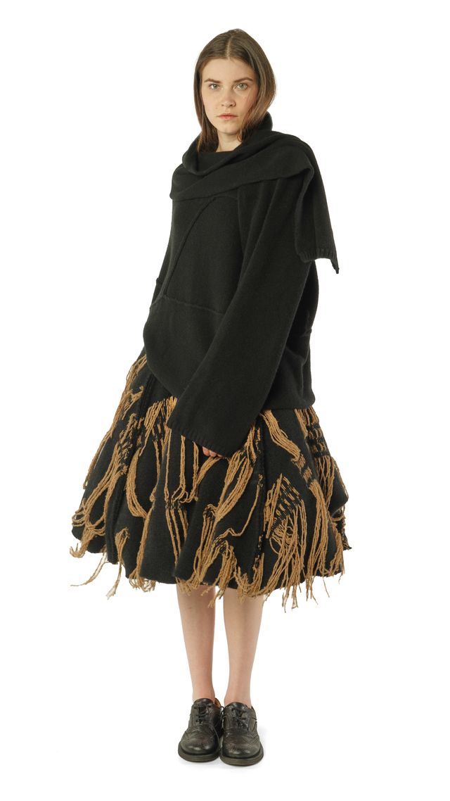 Frau trägt oversized schwarzen Pulli mit Fransenrock und schwarzen Stiefeln.