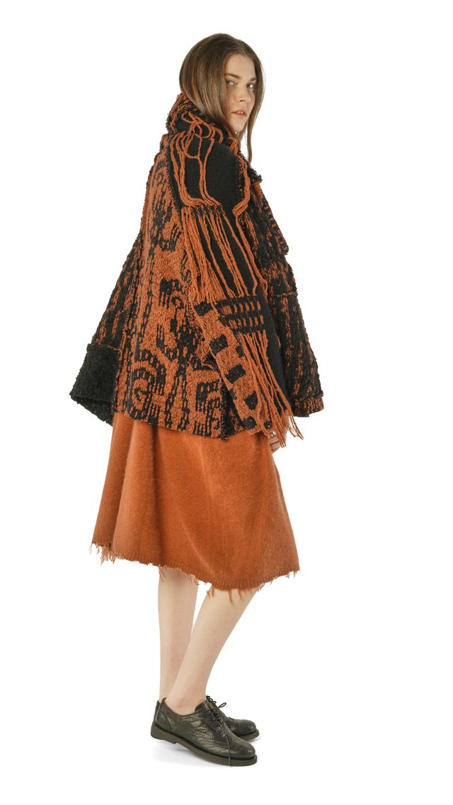 Person trägt bunte, gemusterte Poncho-Jacke mit orangefarbenem Rock und schwarzen Schuhen.