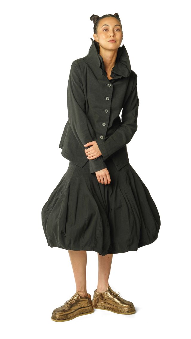 Frau trägt oversized schwarzen Mantel mit weitem Rock und braunen Stiefeln, lässig stehend.