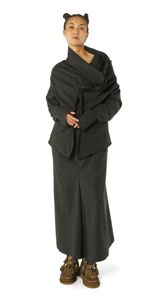 Person trägt eleganten schwarzen oversized Mantel mit langen Stiefeln, Hände vor dem Körper.