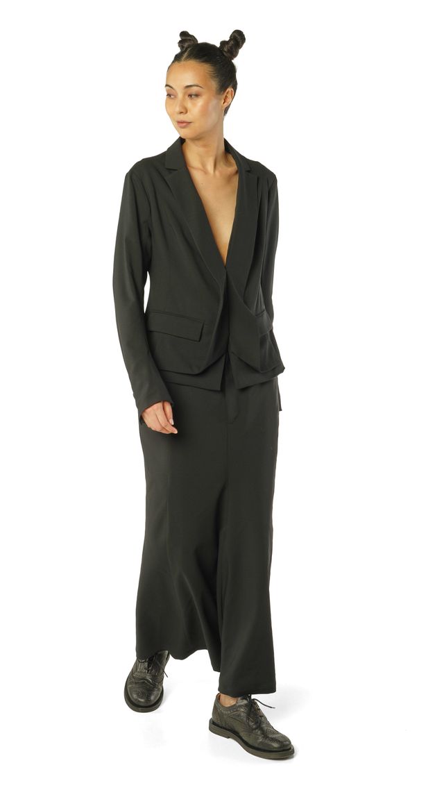Frau trägt elegantes schwarzes oversized Blazer-Set mit weitem Hosenrock und Sneakern.