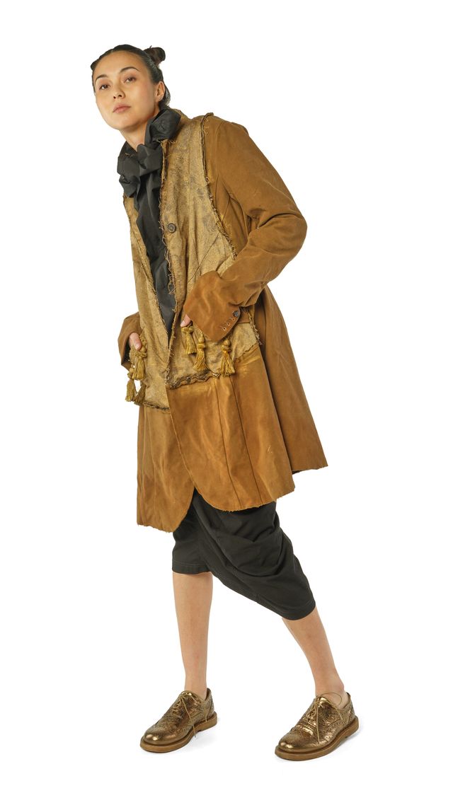 Person trägt langen, gold-bordierten Mantel mit schwarzen Hosen und glänzenden Schuhen.