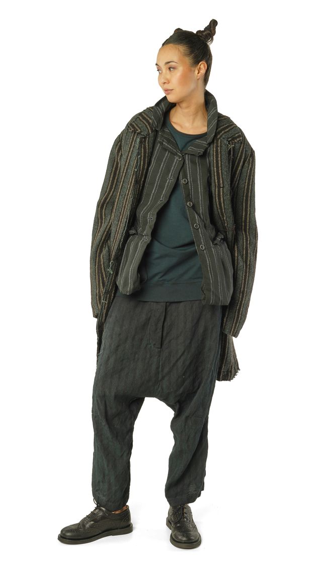Frau trägt oversized gestrickte Jacke mit Fransen, schwarze Haremhose und dunkle Stiefel.