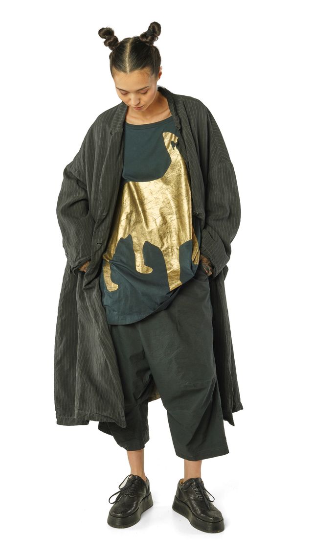 Person trägt oversized Jacke mit goldener Katzen-Applikation, schwarze Hose und Sneaker, Haare zu Buns gebunden.