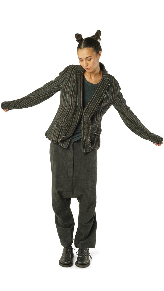 Frau in gestricktem Cardigan und weiten Hosen, Arme ausgebreitet, mit bunten Haargummis.
