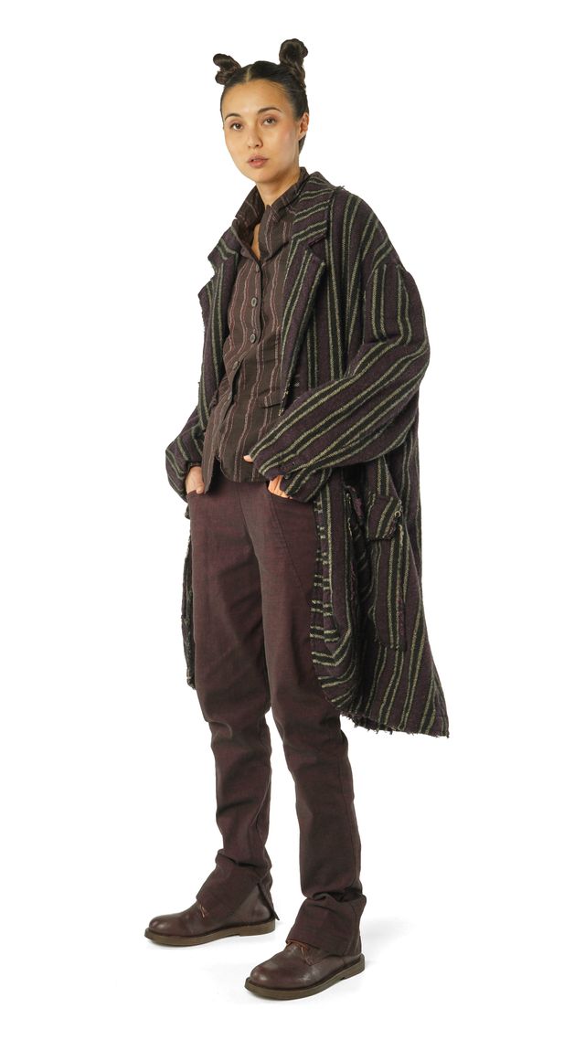 Person trägt oversized gestreifte Jacke, dunkle Hose und Stiefel mit zwei kleinen Haarbändern.