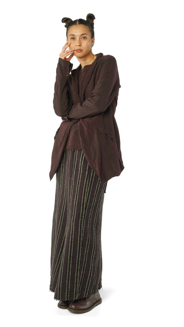 Person in braunem oversized Shirt, gestreifter Hose und nachdenklichem Pose.
