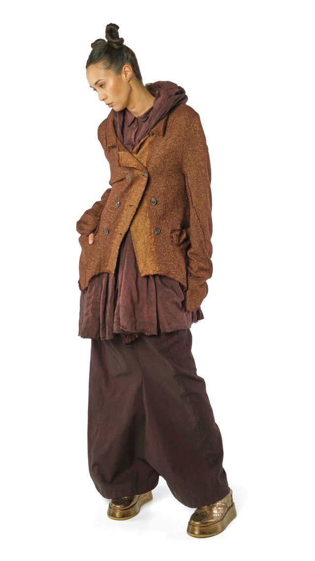 Person trägt oversized braunen Mantel mit weitem Rock und bequemen Hosen, barfuß mit Socken.