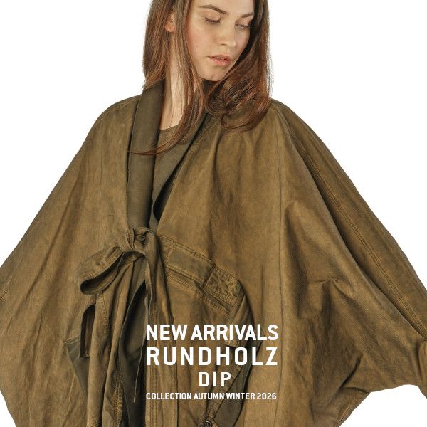 Frau trägt olivfarbenen Rundholz-Dip-Mantel aus der Herbst-Winter-Kollektion 2026.